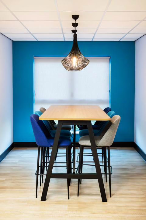 Modern kitchen and refreshment area with a white countertop, hanging blue pendant lights, and a back wall with a sink and beverage station. Minimalist and welcoming design.