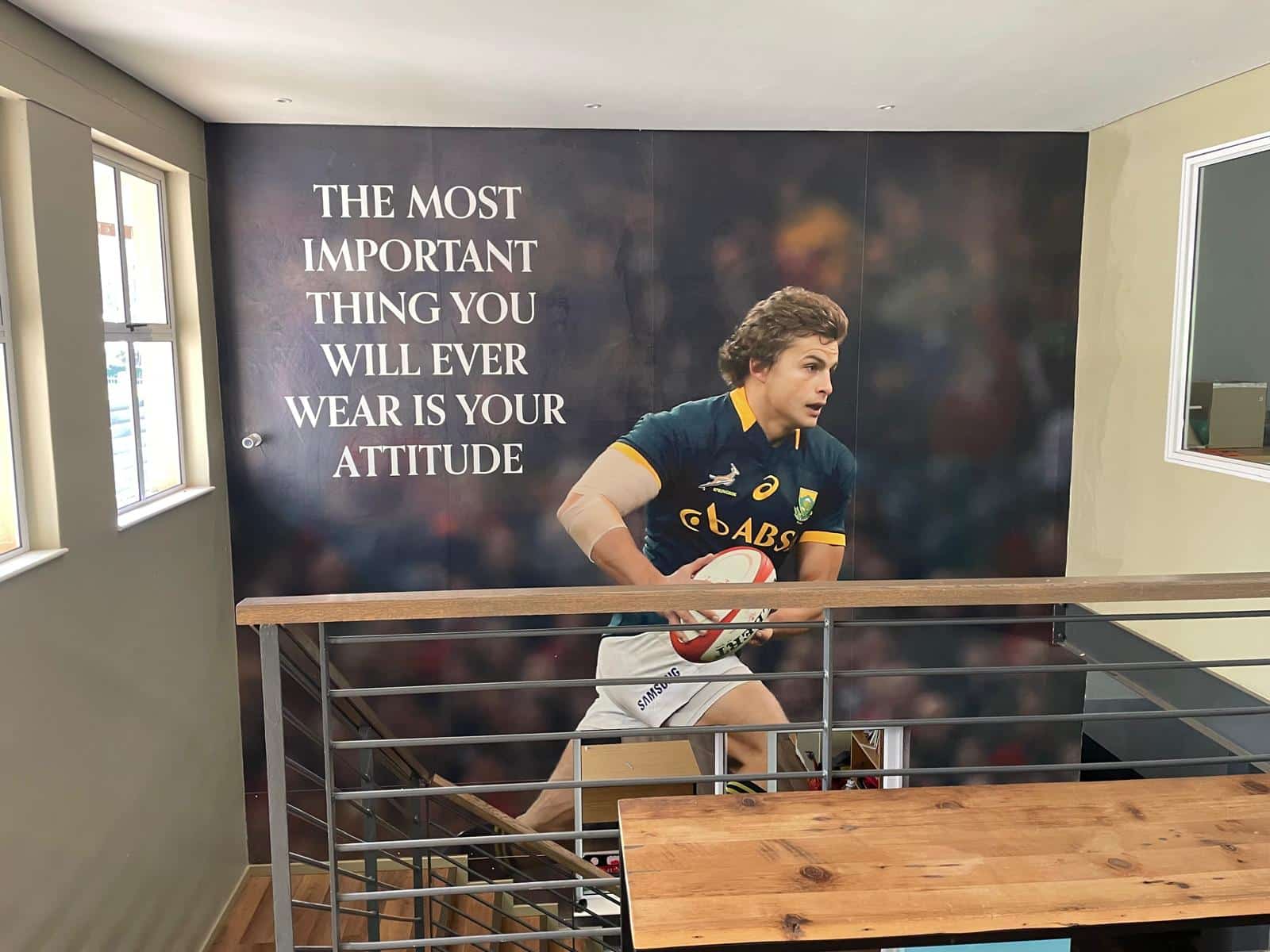 An indoor wall mural of a rugby player in a South African jersey holding a ball, with the quote: 