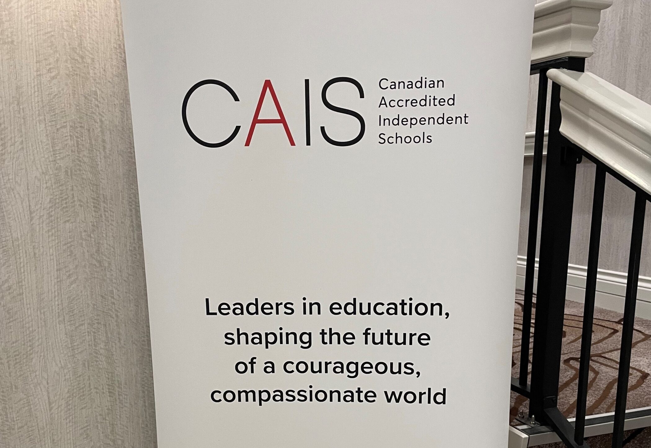 Banner for Canadian Accredited Independent Schools (CAIS) reading “Leaders in education, shaping the future of a courageous, compassionate world,” displayed in a hotel hallway.