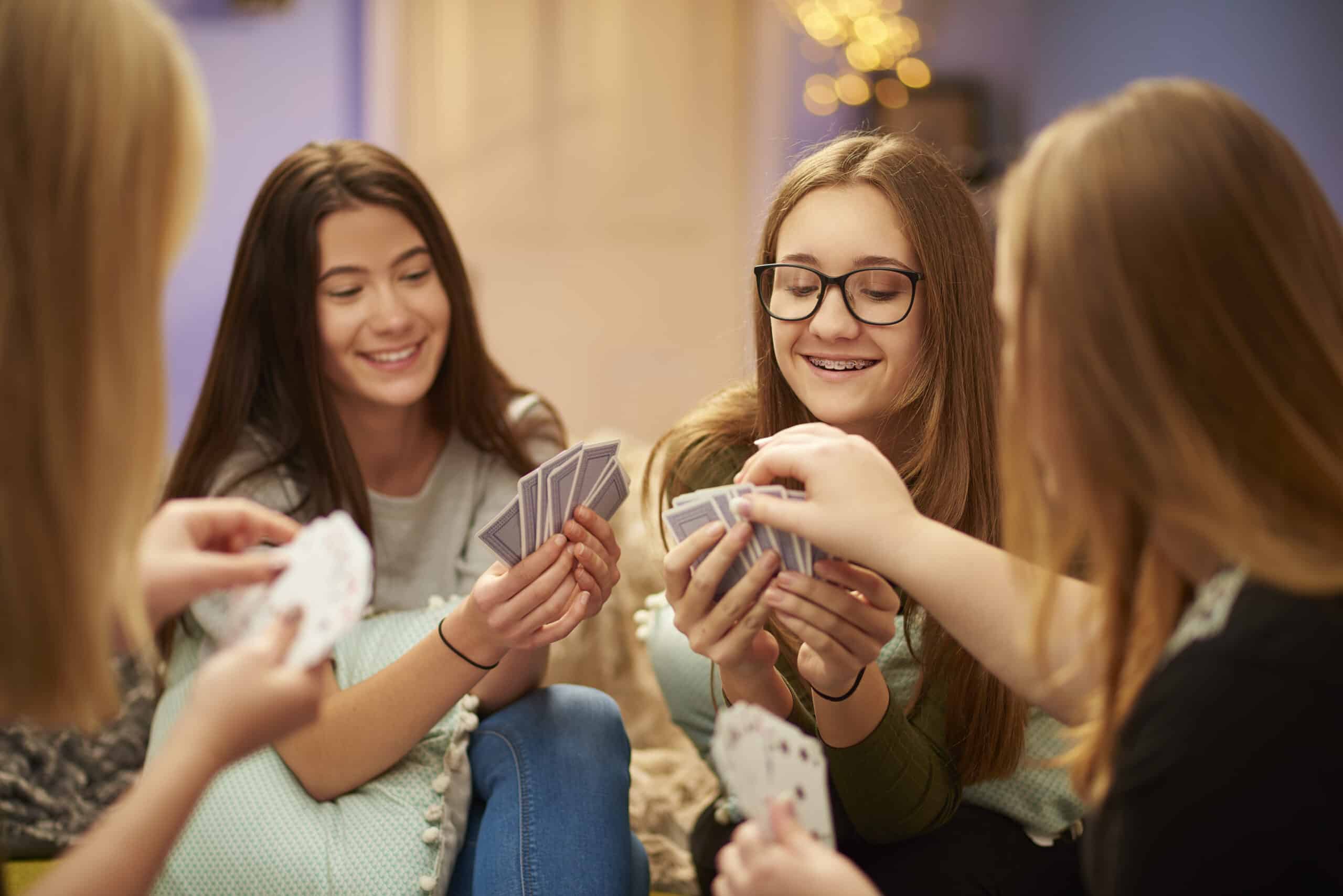 A group of four teenage girls sit at home and play a game of cards.