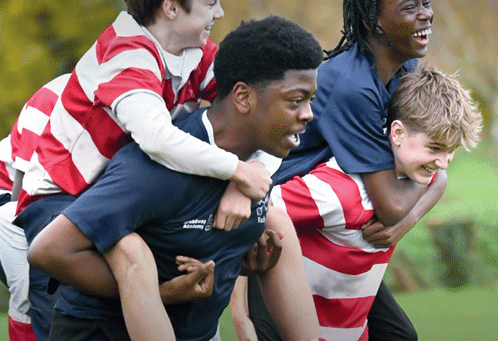 A group of school students are outdoors, smiling and laughing while playing a piggyback race. Two students in dark blue sports uniforms are carrying teammates in red and white striped rugby shirts. The background shows a grassy field with trees. The text reads “Celebrating Partnerships,” and the logo of the Independent Schools Council appears in the lower left corner. The issue number “Issue 10” is in the bottom right.